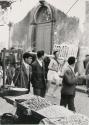 Men walking past flea market, barefoot man in shorts running with wood plank on shoulder