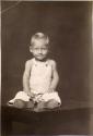 Little boy in overalls seated on table